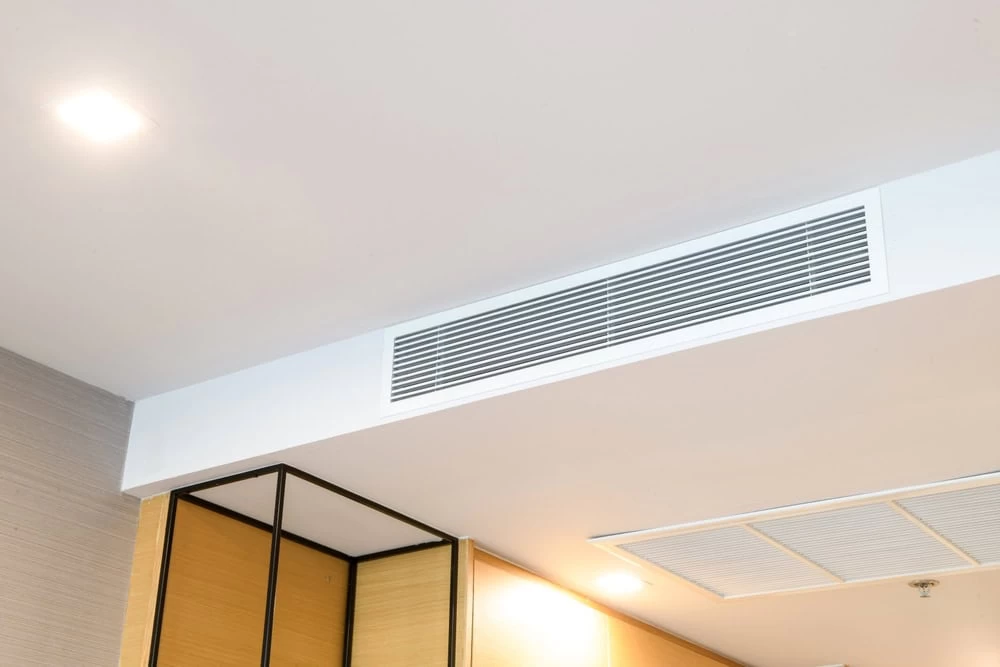 A modern ceiling with recessed lighting and an air conditioning vent. The ceiling is white with a sleek, built-in rectangular vent, and a section features wooden panels with black trim. For optimal performance, consider HVAC Cleaning Sacramento to maintain its contemporary and clean design.