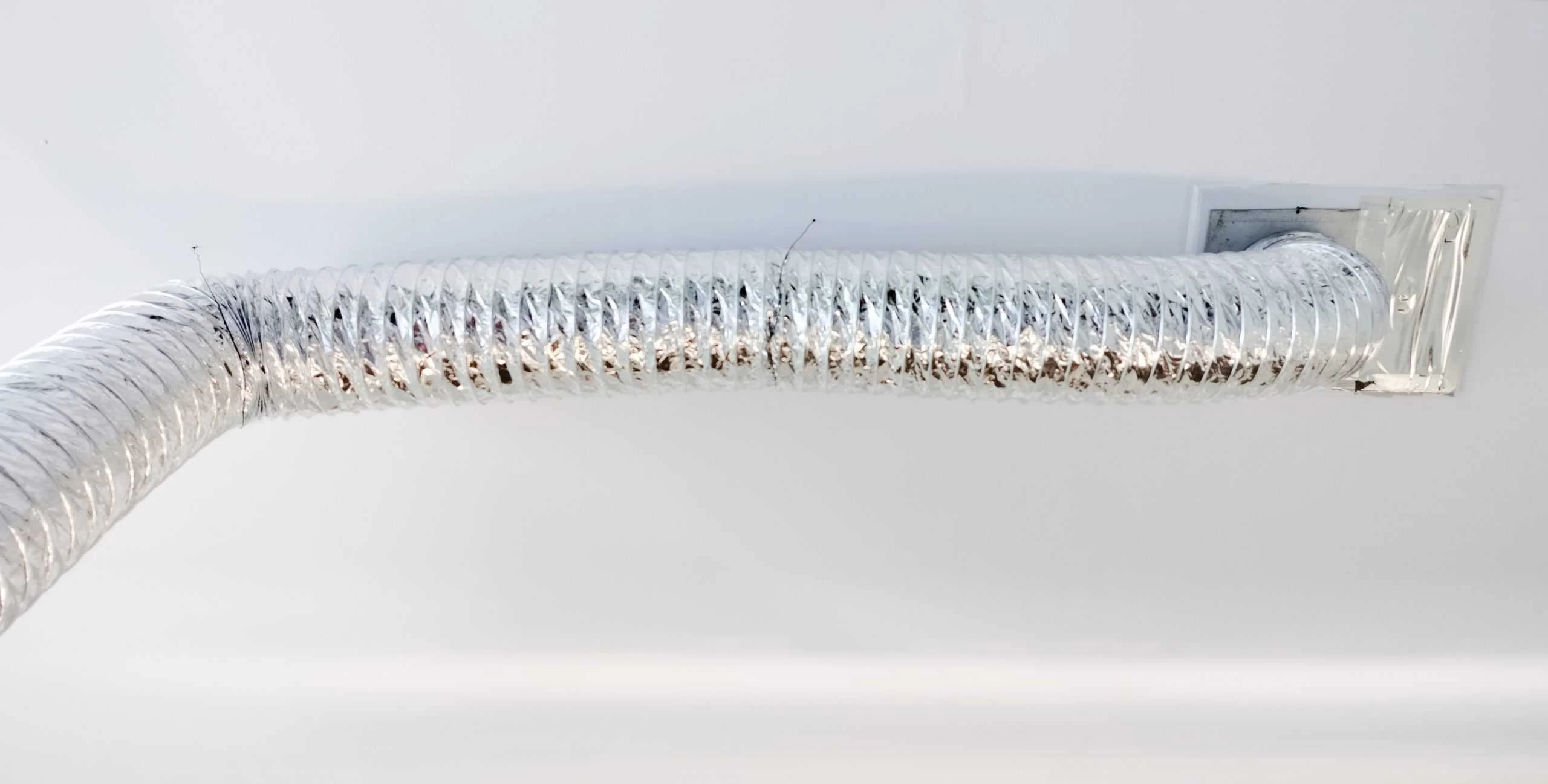 A flexible, silver air duct is attached to the ceiling, extending from a rectangular vent on the right and curving towards the left. The background is a clean, white surface, demonstrating the meticulous results of an Air Duct Cleaning Sacramento service.