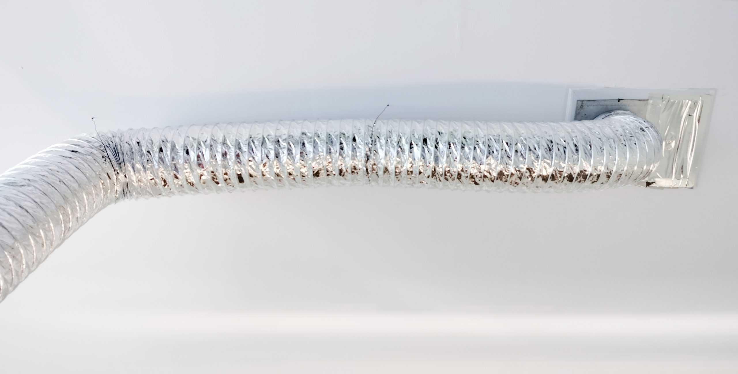 A flexible, silver air duct is attached to the ceiling, extending from a rectangular vent on the right and curving towards the left. The background is a clean, white surface, demonstrating the meticulous results of an Air Duct Cleaning Sacramento service.
