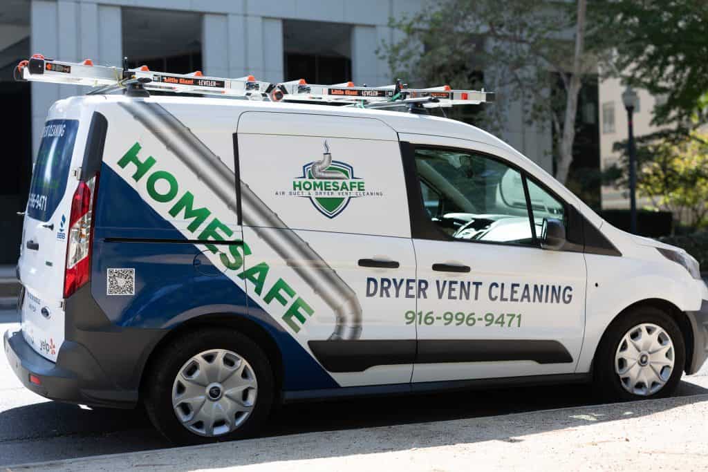 A white van with "HOMESAFE Dryer Vent Cleaning" written on the side, featuring a phone number (916-584-9367). The vehicle displays a green and blue logo, a QR code, and has ladders mounted on the roof. The background shows trees and buildings — perfect for all your ventilation system cleaning needs.