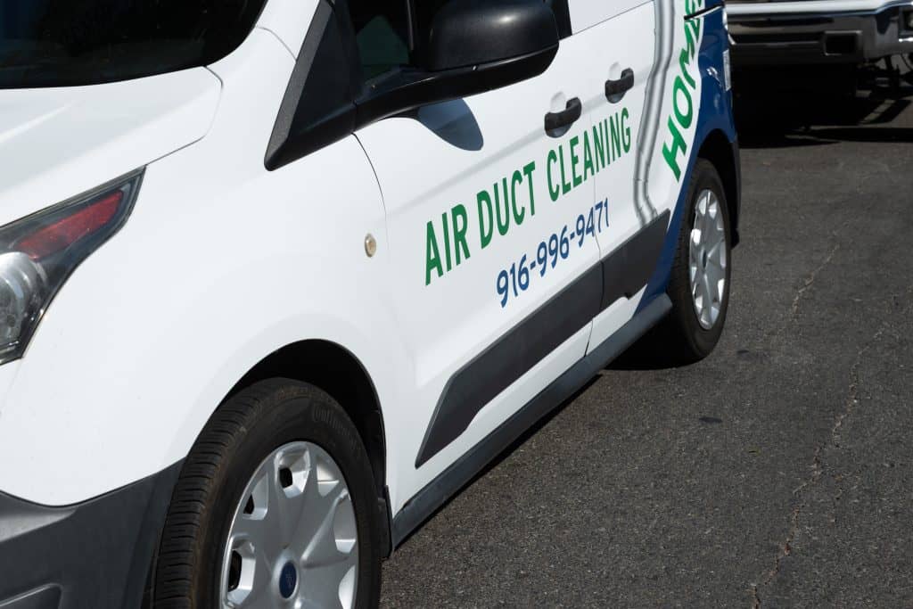 A white van with the text "AIR DUCT CLEANING" and a phone number "916-584-9367" displayed on its side panel. The van, specializing in HVAC system maintenance, is parked on a paved surface with part of another vehicle visible in the background.