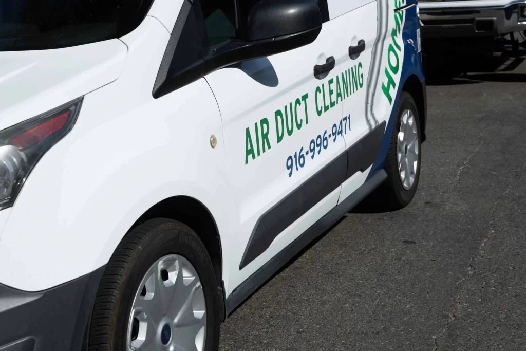 A white van with the text "AIR DUCT CLEANING" and a phone number "916-288-9562" displayed on its side panel. The van, specializing in HVAC system maintenance, is parked on a paved surface with part of another vehicle visible in the background.
