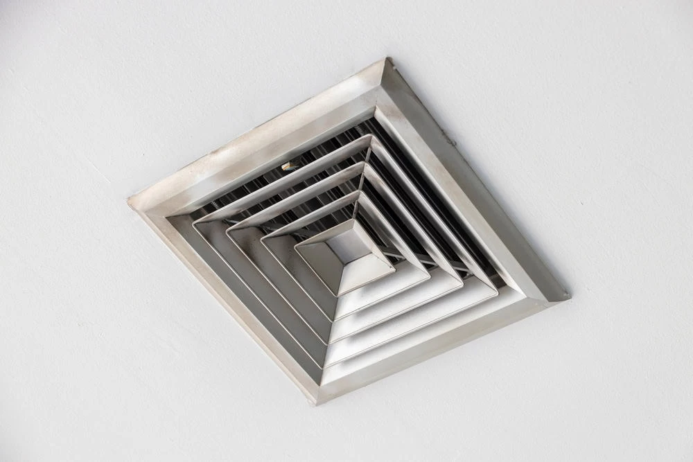 A square, silver ceiling air vent with concentric square layers is shown against a white ceiling background.