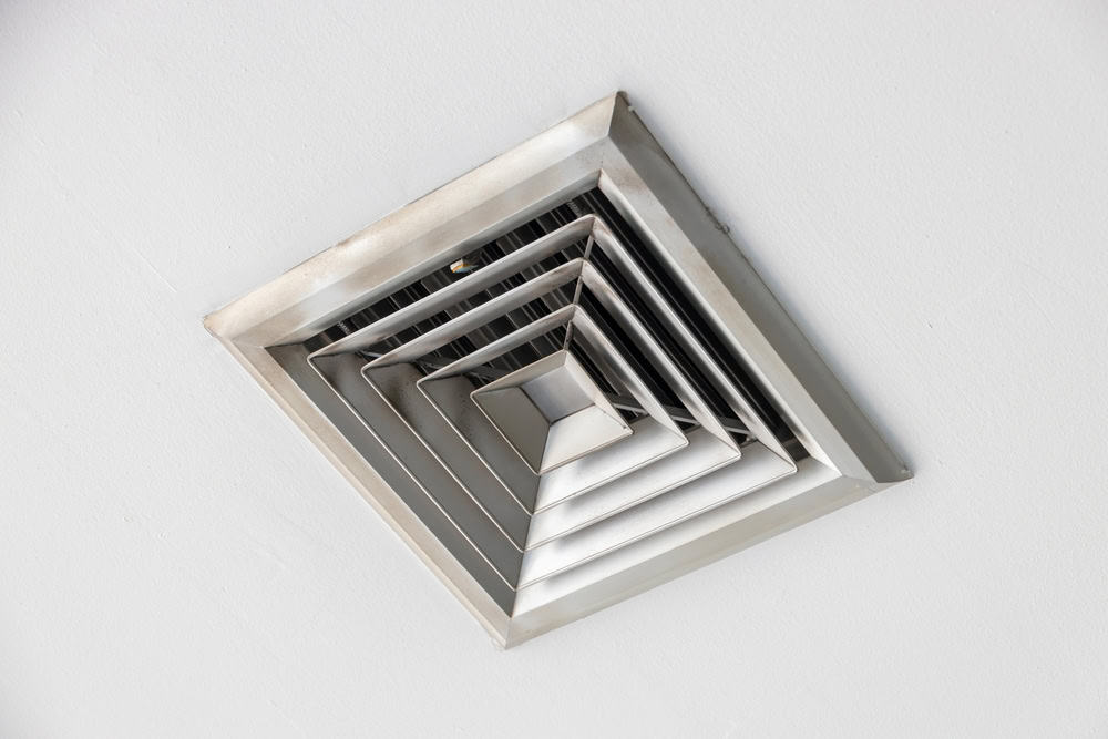 A square, silver ceiling air vent with concentric square layers is shown against a white ceiling background.
