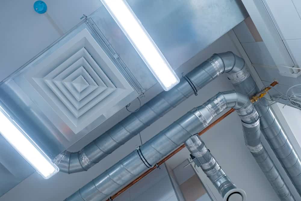 Ceiling view displaying exposed silver ventilation ducts and rectangular fluorescent light fixtures in an industrial or commercial setting.