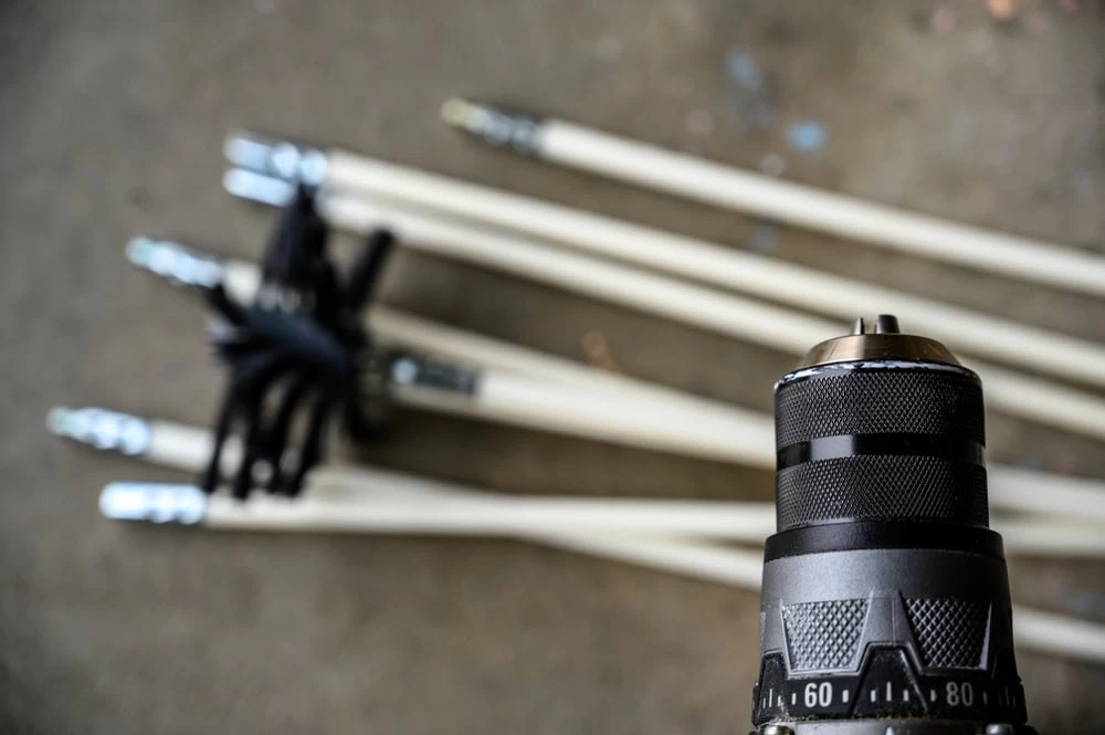 Close-up of a drill chuck in focus with several long, white extension rods lying on the ground in the background, slightly out of focus.