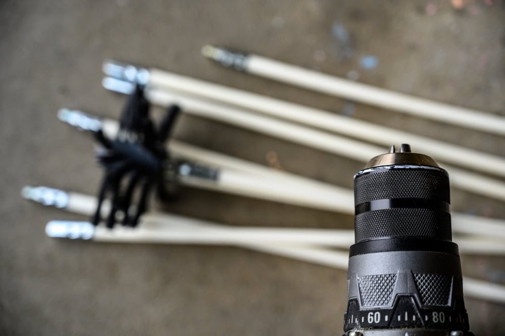Close-up of a drill chuck in focus with several long, white extension rods lying on the ground in the background, slightly out of focus.